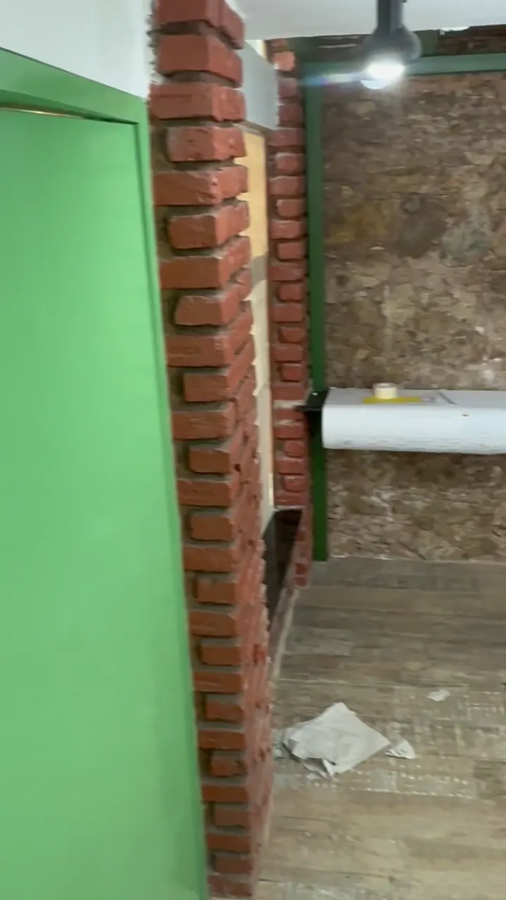 Parede de pedra com coluna de tijolo, piso de madeira gasto e entulho no chão