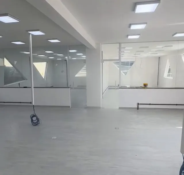 Salão vazio com piso cinza, luminárias e divisórias de vidro antes da obra