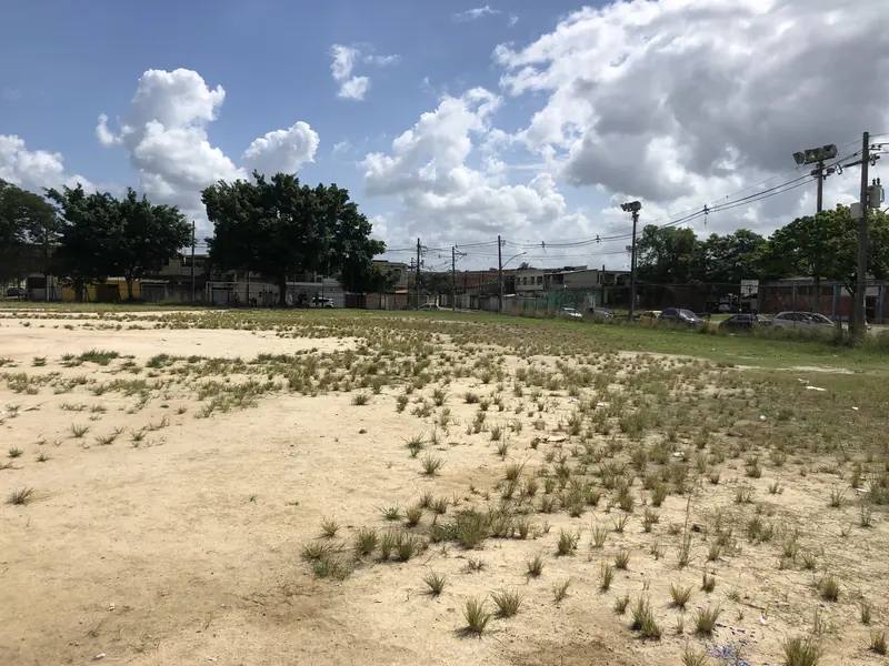 Campo de terra batida com mato ralo antes da obra