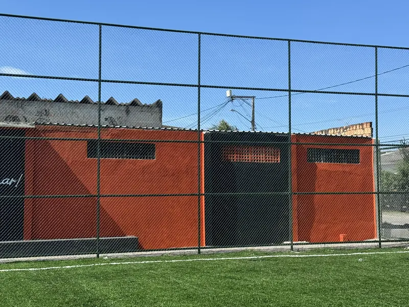 Muro recuperado pintado de laranja e preto atrás do alambrado