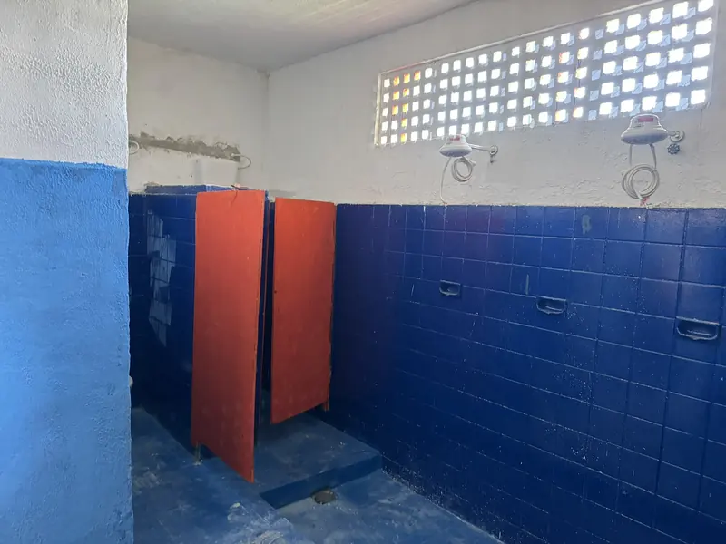Vestiário com azulejo azul, divisórias laranja e chuveiros